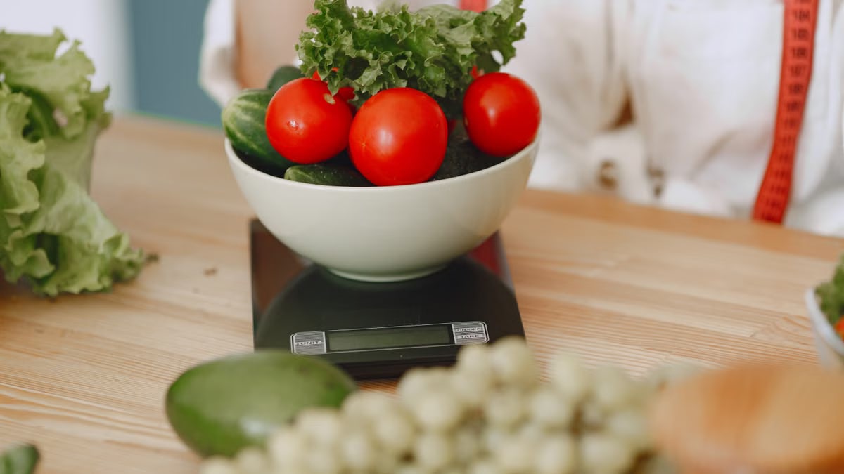 Colorful fresh vegetables including tomatoes and cucumbers on a kitchen scale for healthy eating.